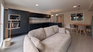 Una cocina moderna con armarios oscuros, horno empotrado y comedor con mesa y sillas de madera.