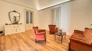 A spacious living room with a wooden floor, a white console table, a pink armchair, a brown armchair, and a brown sofa. - Dimore del Plebiscito B&B (Catania)