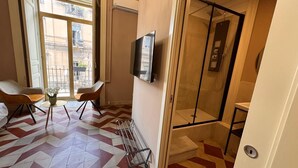 A modern bathroom with a shower, a toilet, and a sink. There is a TV mounted on the wall and a chair in the corner. - Dimore del Plebiscito B&B (Catania)