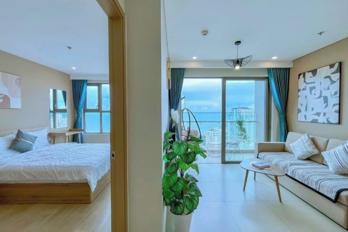 A modern hotel room with a bed, a sofa, a coffee table, and a large window offering a view of the city.