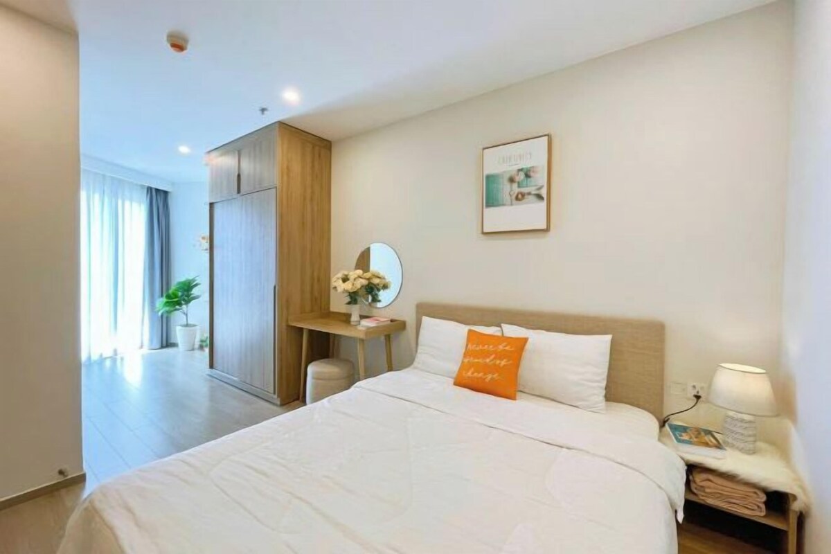 A hotel room with a large bed, a bedside table with a lamp, a small desk with a mirror, and a framed picture on the wall.
