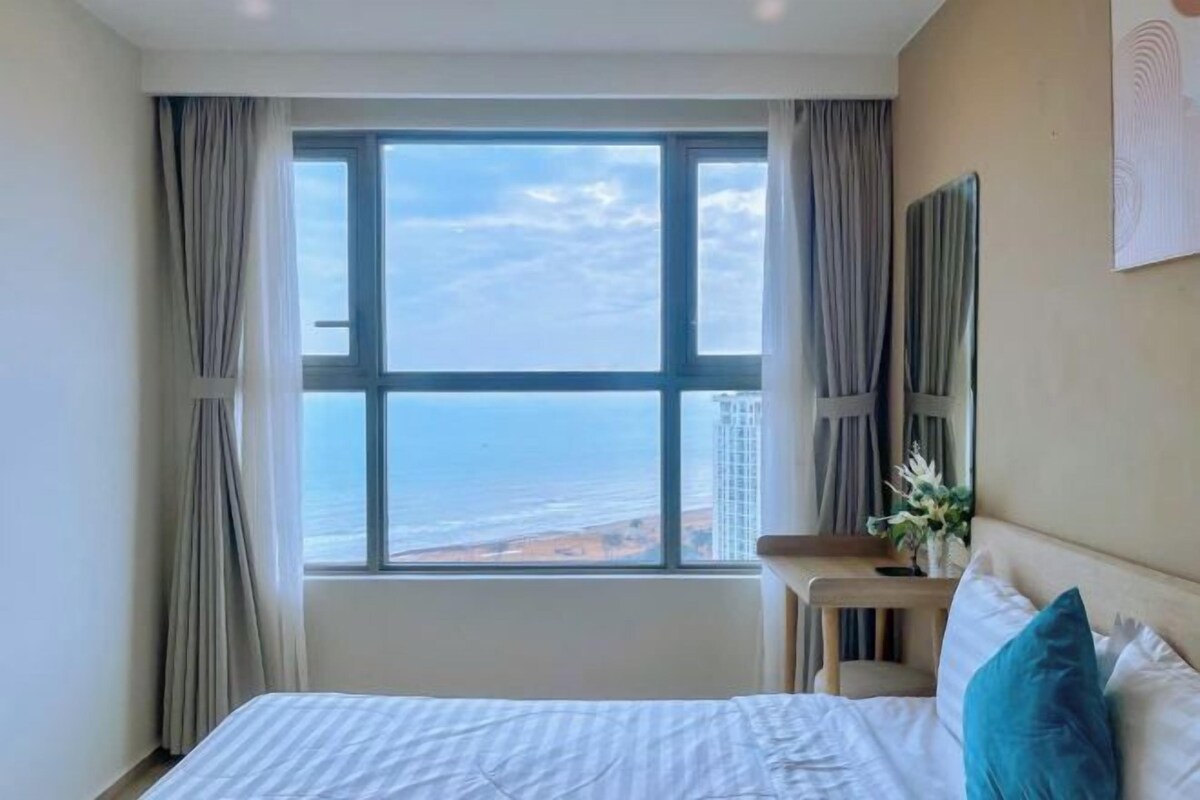 A hotel room with a large window offering a view of the ocean and a building.