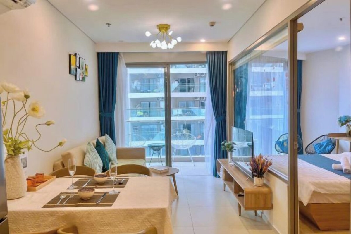 A modern hotel room with a dining area, a bed, a TV, and a balcony with a view of the city.