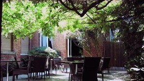 An outdoor patio area with a brick wall, a table, and chairs. - The Venice Times (Venice)