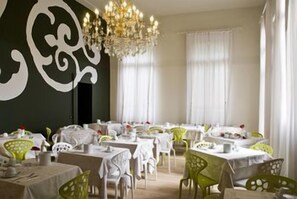 A dining area with tables and chairs, a chandelier, and a green wall with a white design. - The Venice Times Hotel, Vignette Collection by IHG (Venice)