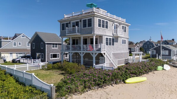 A multi-story building with a balcony, surrounded by a white fence and beachside vegetation.