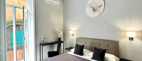 A bedroom with a large bed, a desk, a chair, and a view of the outside.