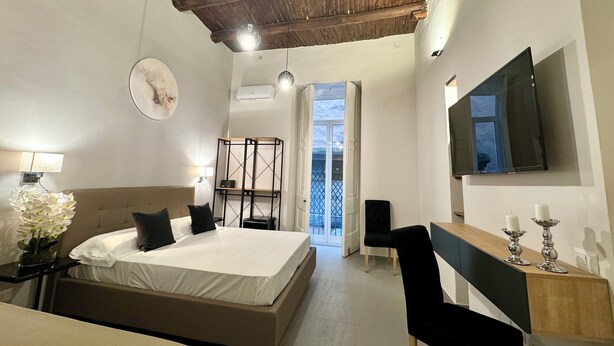 Un dormitorio con cama, mesita de noche, lámpara y televisor montado en la pared.