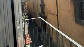 Un estrecho callejón con barandilla de metal, una pequeña ventana con celosía y una bandera colgada en la pared.
