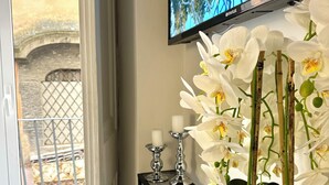 Una habitación con un televisor montado en la pared, una mesita consola con un control remoto y una orquídea en maceta.