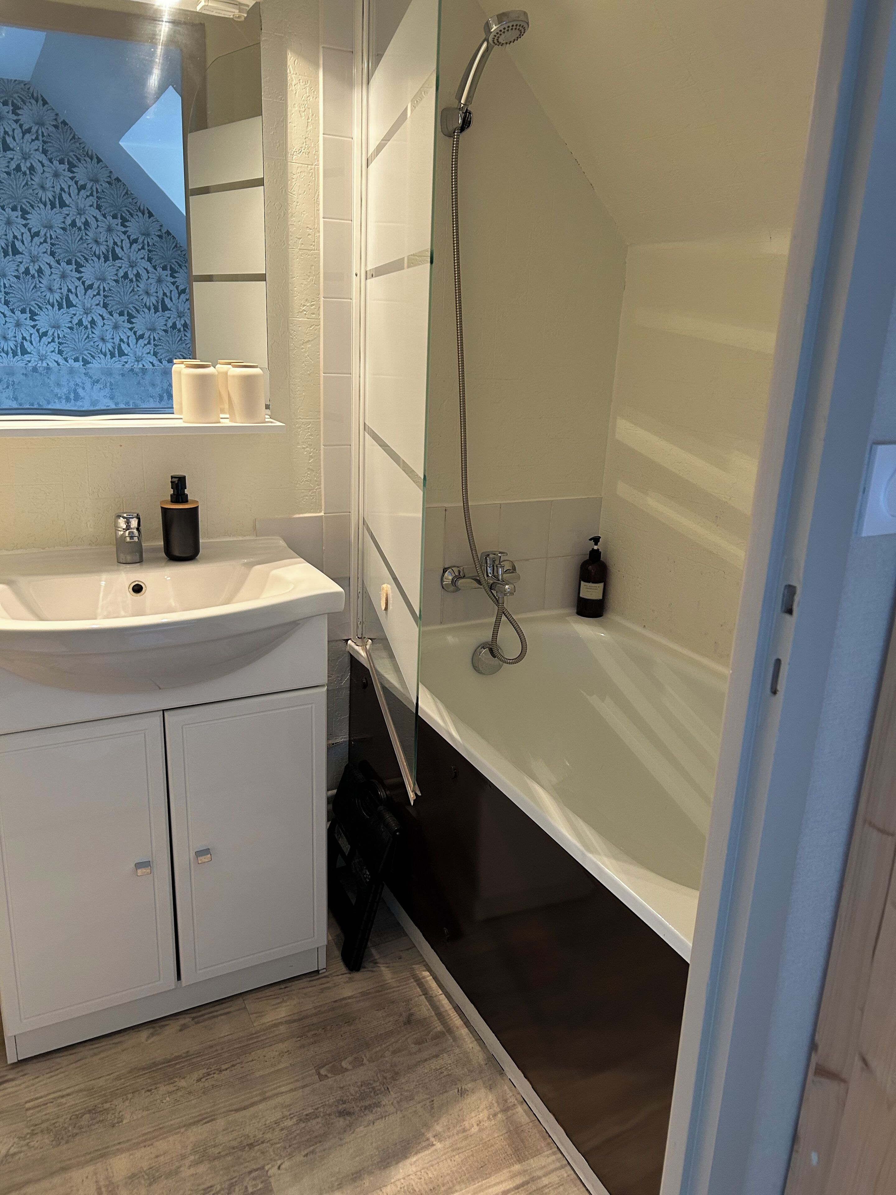 Ein modernes Badezimmer mit Duschkabine aus Glas, einem weißen Waschbecken mit Spiegel darüber und Holzboden.