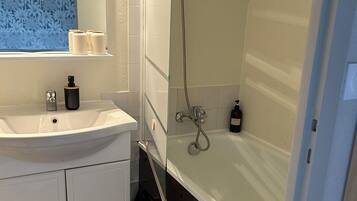 Ein modernes Badezimmer mit Duschkabine aus Glas, einem weißen Waschbecken mit Spiegel darüber und Holzboden.