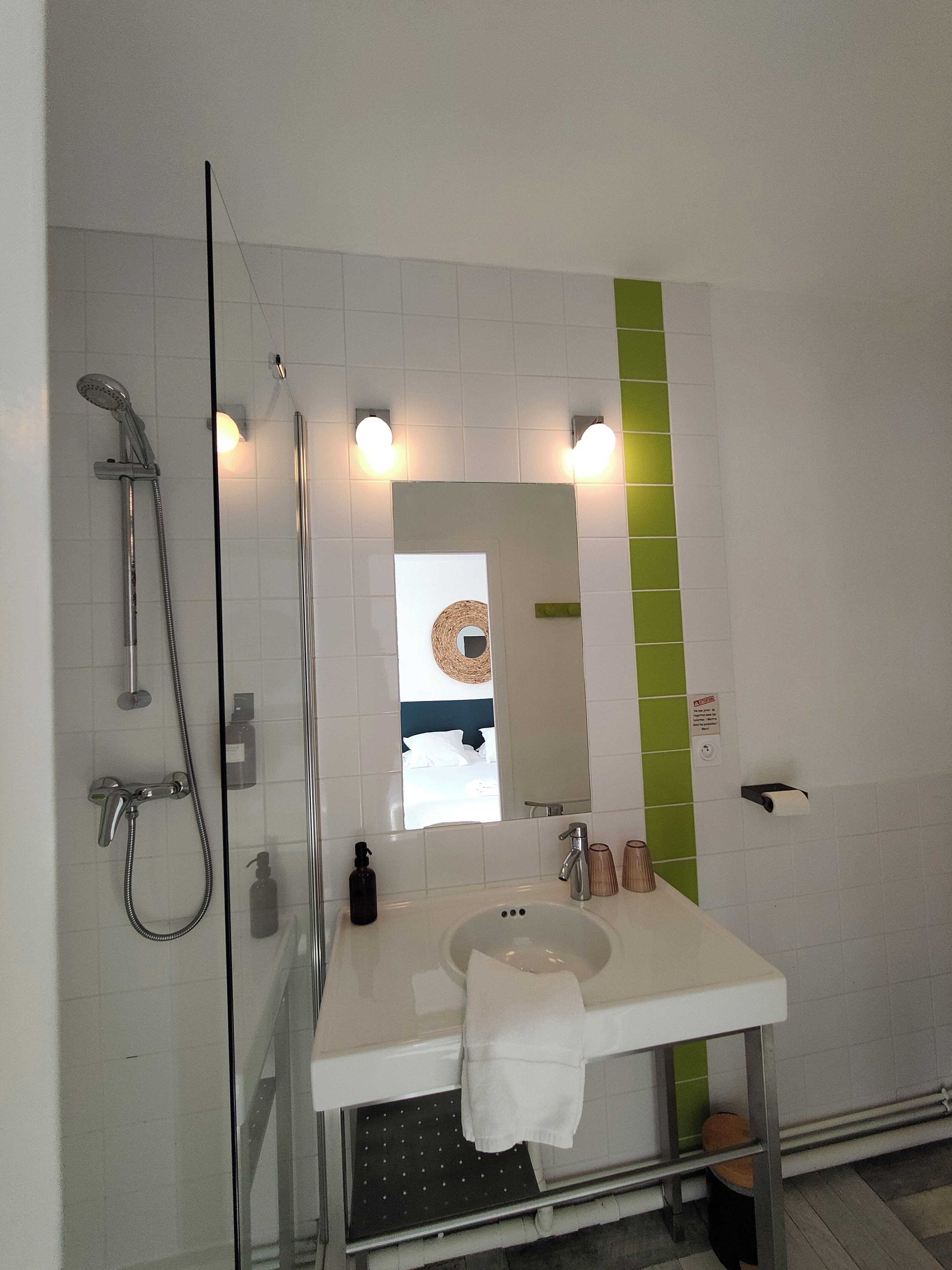 Ein modernes Badezimmer mit Duschkabine aus Glas, einem weißen Waschbecken mit Spiegel darüber und einer Wand in Grünton.