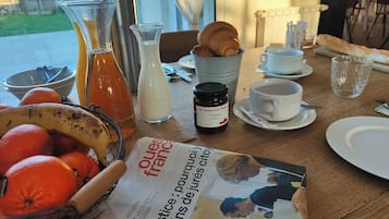 Una mesa de desayuno con cruasanes, naranjas, un periódico, una botella de jugo y un frasco de mermelada.