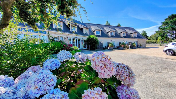 Un hotel con varios pisos, zona de estacionamiento y un jardín con flores de hortensia.