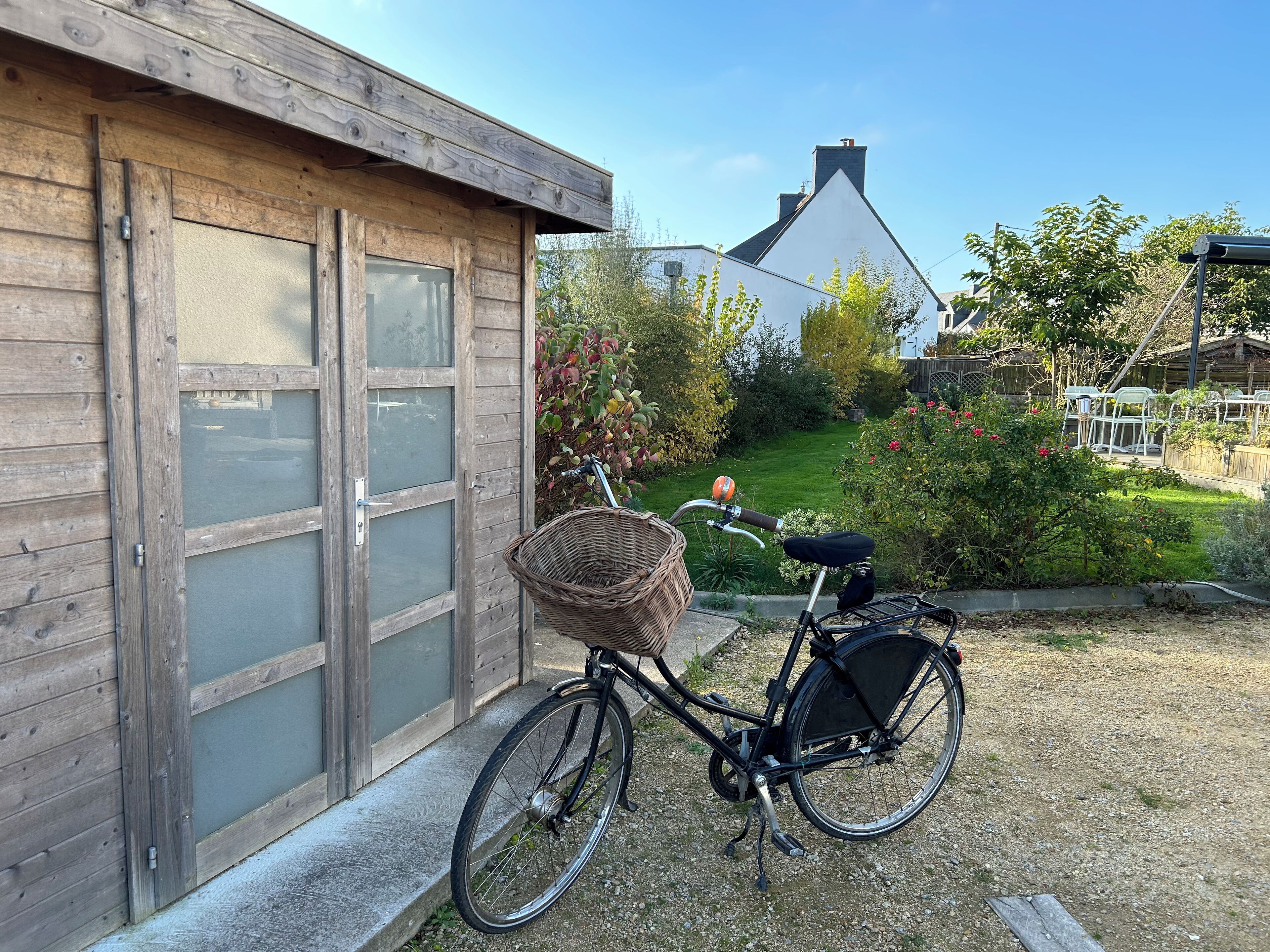 Ein Fahrrad mit Korb steht vor einem Holzhaus mit einer Garagentür.