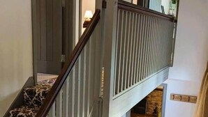 Un interior de varios niveles con una escalera, una pequeña mesa con lámpara y vistas a otra habitación.