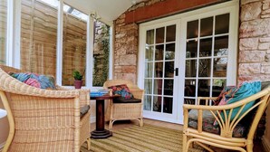 Un patio cubierto con mobiliario de mimbre, una mesa y un muro de piedra.