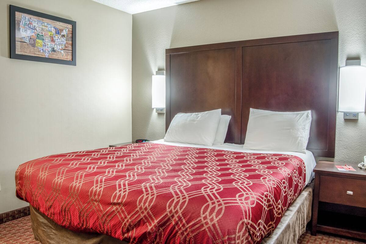 Quarto de hotel com uma cama grande, cabeceira de madeira, duas luminárias laterais e um mapa na parede.