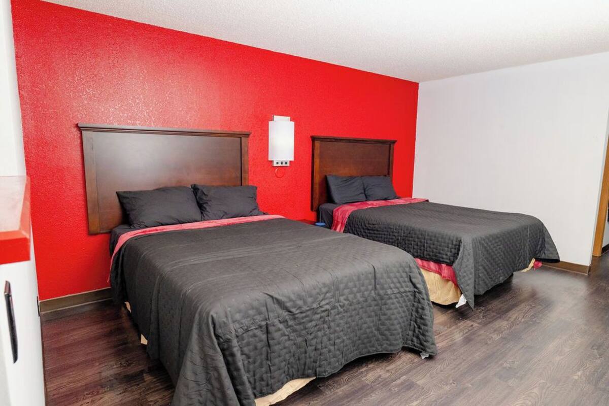 Quarto de hotel com duas camas, paredes vermelhas e chão de madeira.