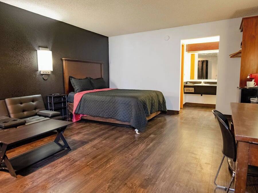 A hotel room with a bed, a sofa, a desk, and a kitchenette.