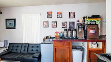 Un espai habitable compacte amb zona de cuina, un sofà de pell negra, nevera petita i cafetera.