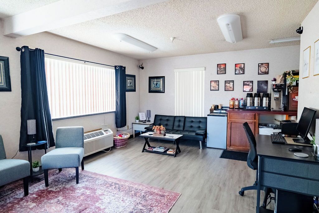 A modern living room with a sofa, a coffee table, a desk with a computer, and a kitchenette area.