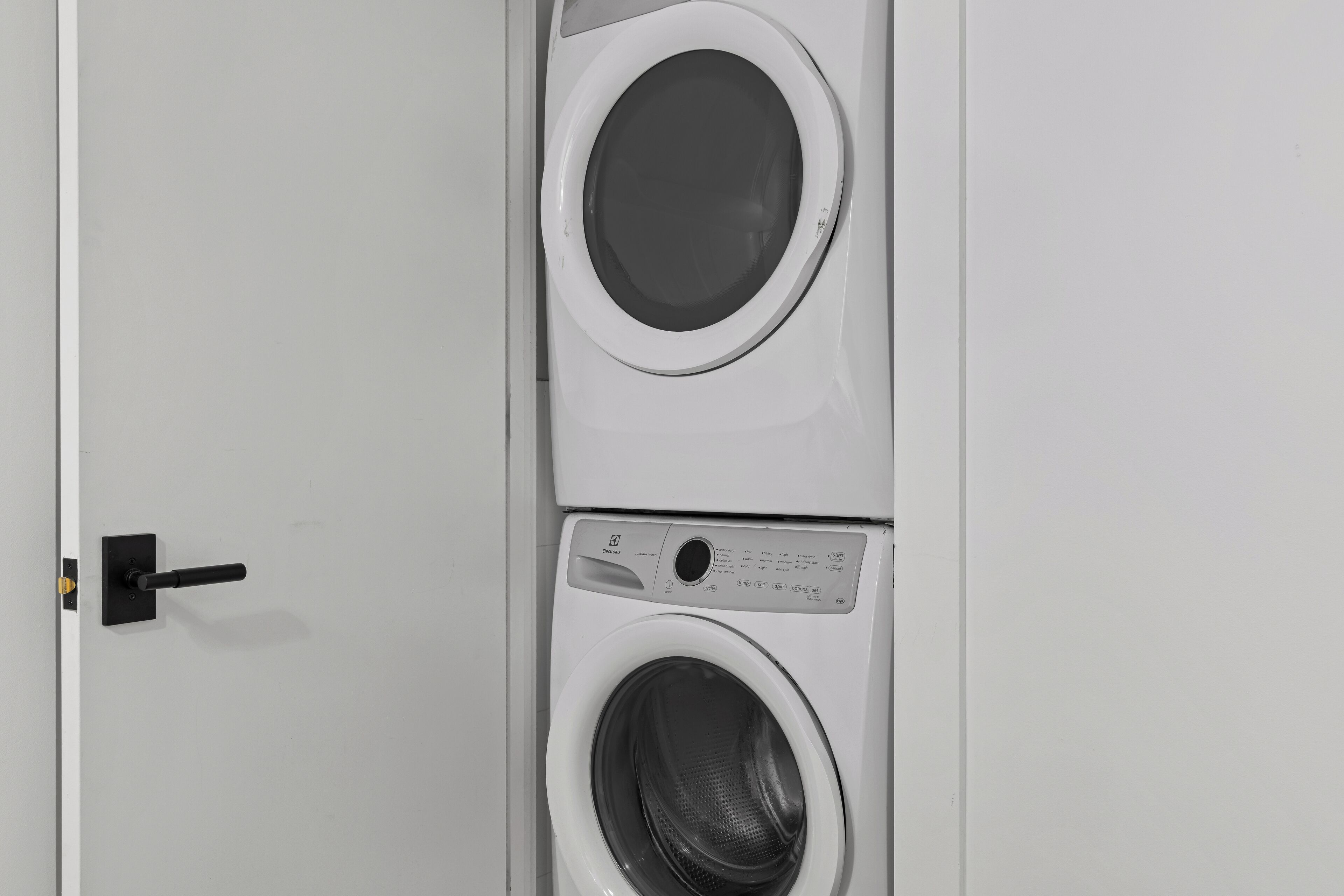 Vista frontal de una lavadora y secadora blancas empotradas en la pared, con un panel de control y un tirador.