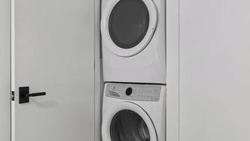 Vista frontal de una lavadora y secadora blancas empotradas en la pared, con un panel de control y un tirador.
