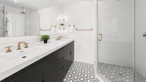 Un baño moderno con un espejo grande, dos lavamanos, ducha y piso estampado.