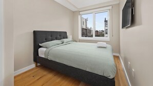 Un dormitorio moderno con una cama grande, un televisor montado en la pared y una ventana con vistas a la ciudad.