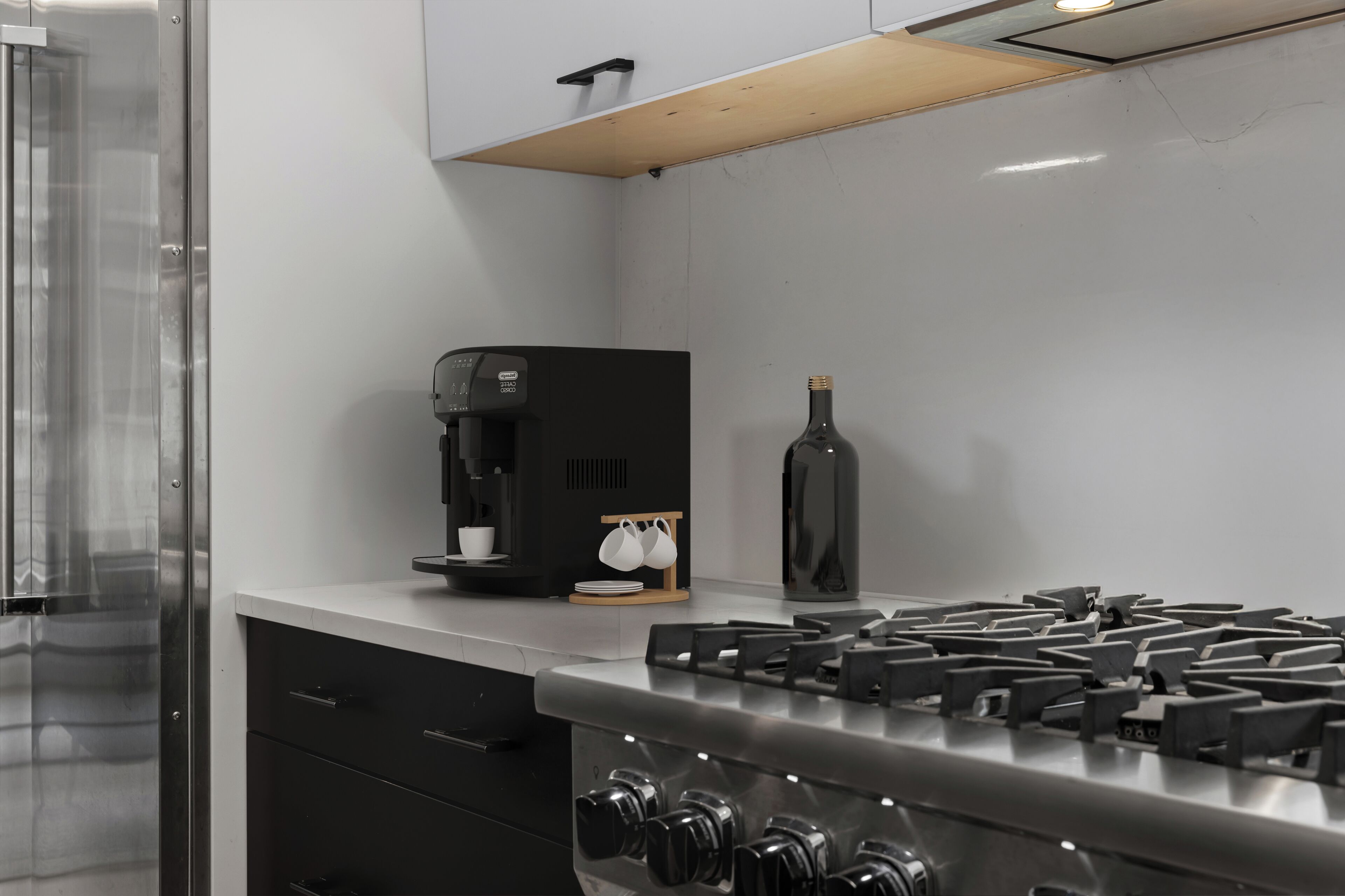 A modern kitchen with a stainless steel stove, a coffee maker, and a wine bottle.