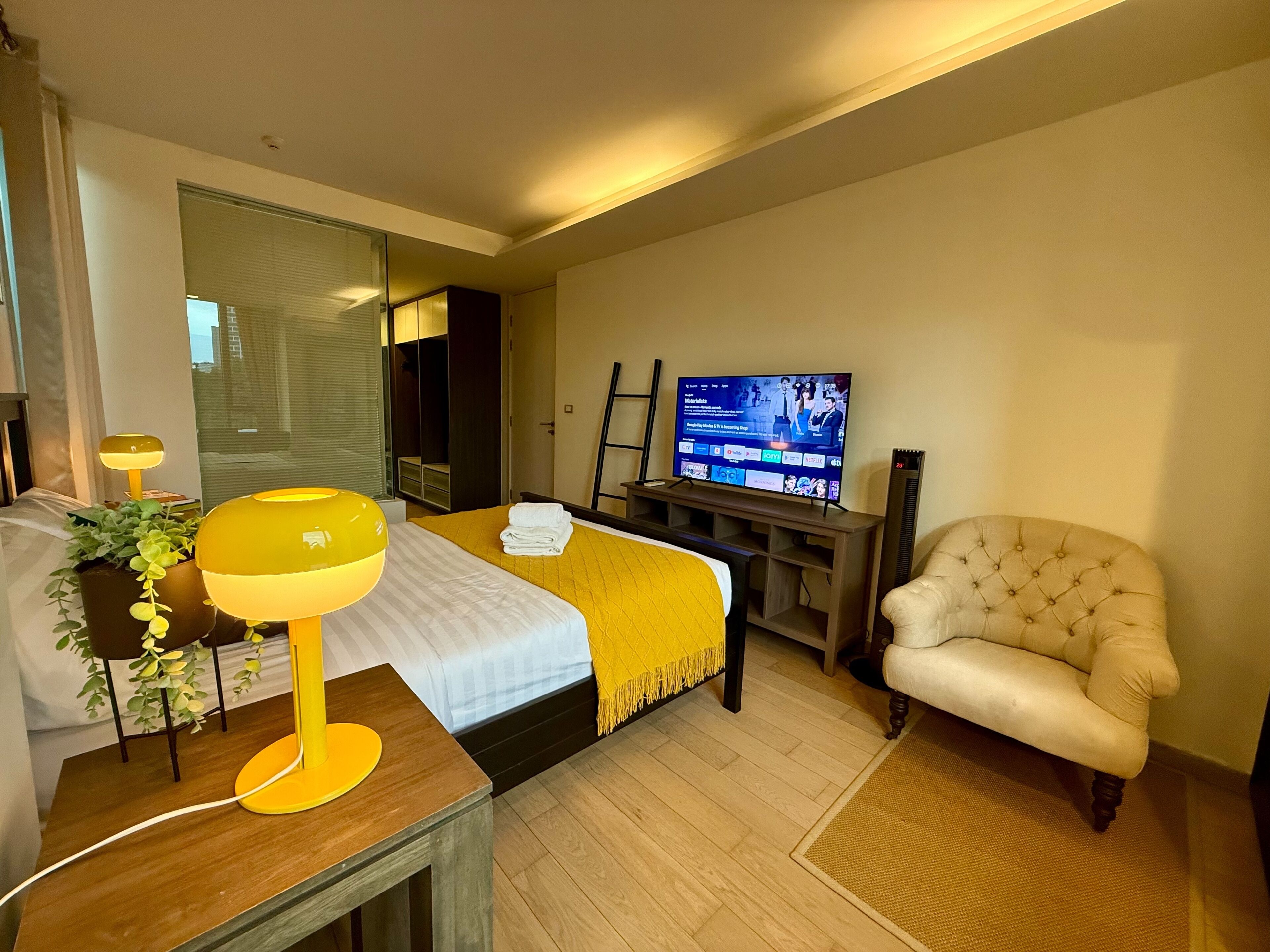 A hotel room with a bed, a television, a chair, and a desk with a lamp.