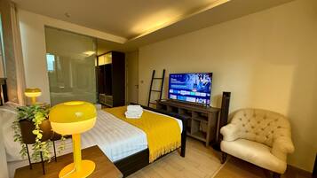 A hotel room with a bed, a television, a chair, and a desk with a lamp.