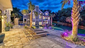 Une maison à deux étages avec une piscine, un espace salon extérieur et des palmiers.