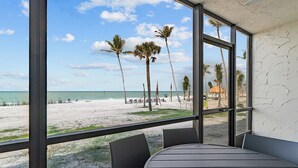 Uitzicht op het strand vanuit een kamer met een tafel, stoelen, grote ramen en een witte muur met structuur.