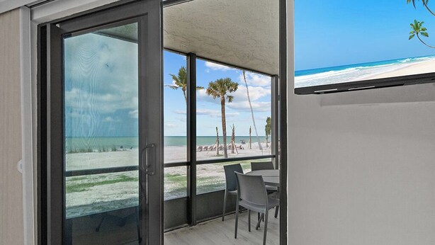 Een moderne kamer met een schuifglazen deur die uitkomt op een balkon met uitzicht op het strand.