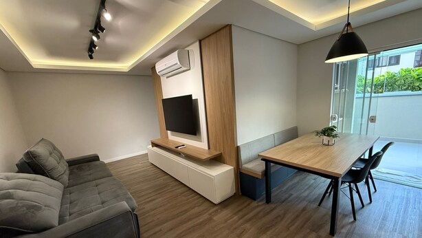 A modern living room with a sofa, TV, dining table, and chairs. - RCM Vilas - Apartamento Sofisticado (Joinville)