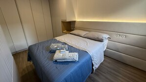 A modern bedroom with a large bed, a nightstand, and a built-in wardrobe. - RCM Vilas - Apartamento Sofisticado (Joinville)
