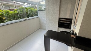 A small balcony with a glass door, a black countertop, and a white tiled floor. - RCM Vilas - Apartamento Sofisticado (Joinville)