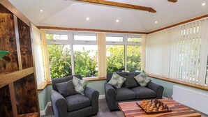 Una habitación acogedora con dos sofás grises, una mesa de centro de madera con un juego de ajedrez y ventanas grandes con persianas.