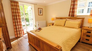 Un dormitorio con cama de madera, dos mesitas de noche con lámparas, una ventana con cortinas y una puerta que da a un área exterior.