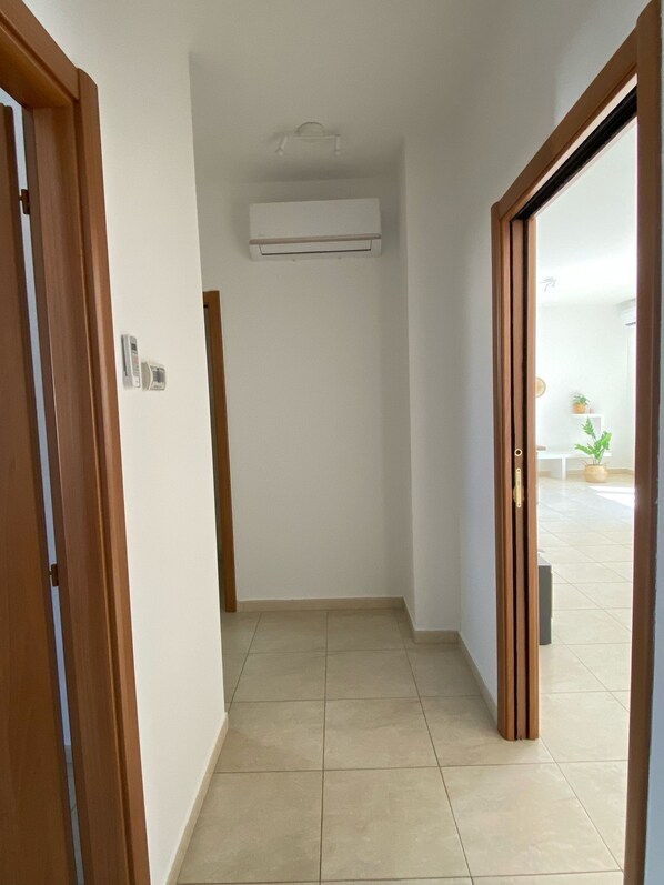 A hallway with a tiled floor, a white wall-mounted air conditioning unit, and a wooden door frame.