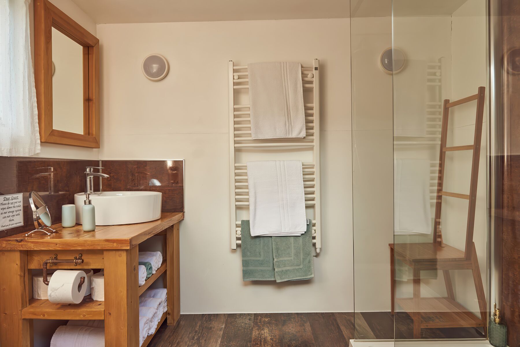 Un baño con tocador de madera, un perchero con dos toallas y una cabina de ducha de vidrio.