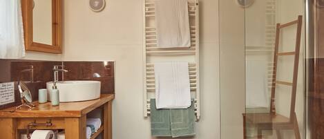 Un baño con tocador de madera, un perchero con dos toallas y una cabina de ducha de vidrio.