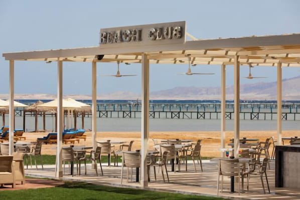 Relax in the shaded outdoor seating area with tables and chairs, taking in the breathtaking views of the beach and sea.