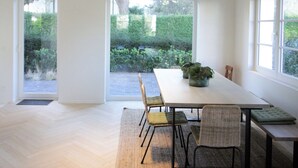 A modern dining room with a large table, chairs, and a view of greenery through large windows. - Villa in Knokke-heist Near the Beach (Knokke-Heist)