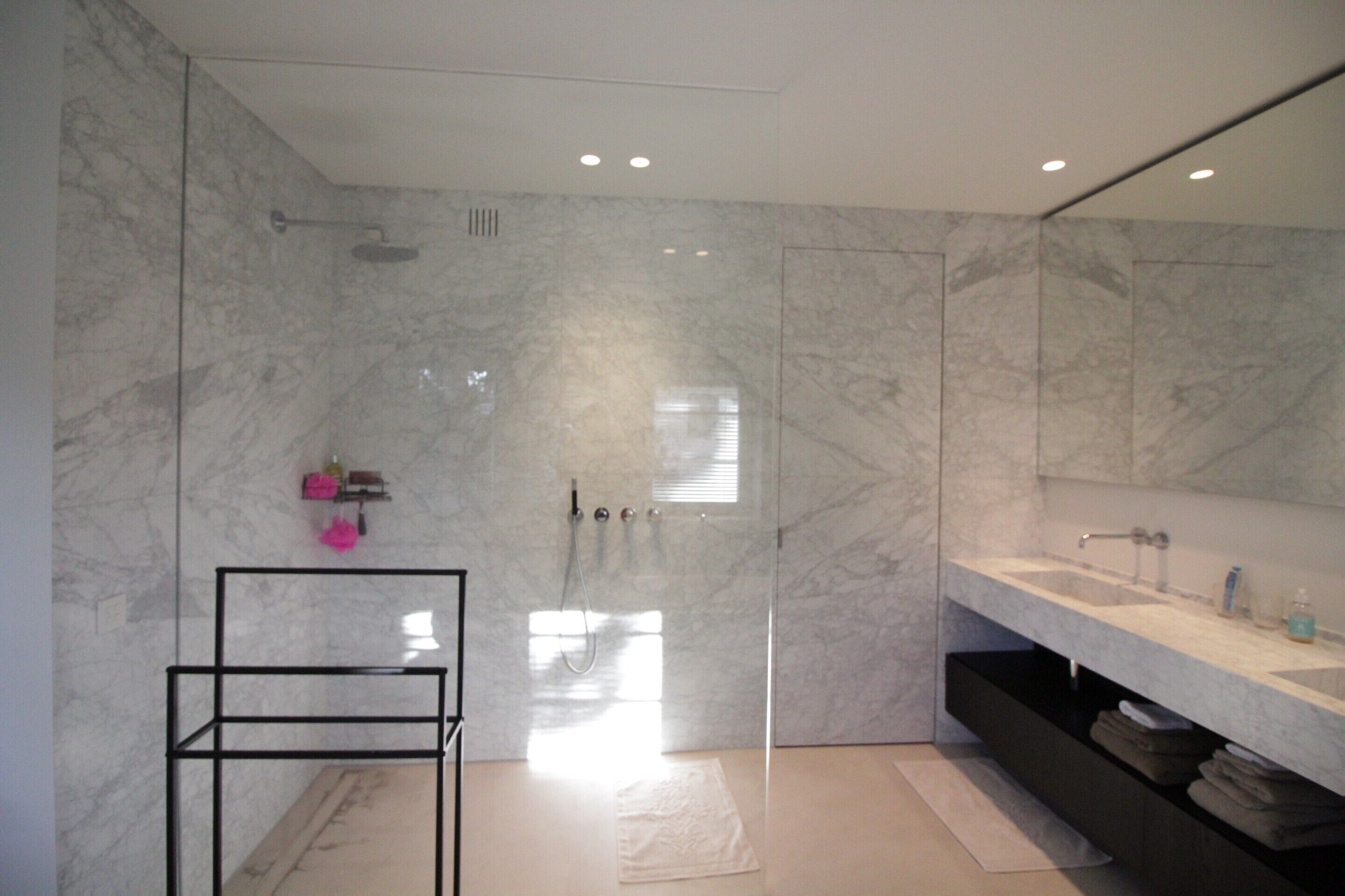 Une salle de bain moderne dotée d’une douche à parois de verre, d’un grand miroir et d’un meuble-lavabo avec un évier et des rangements.
