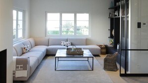 A modern living room with a sectional sofa, a coffee table, and a glass cabinet. - Villa in Knokke-heist Near the Beach (Knokke-Heist)
