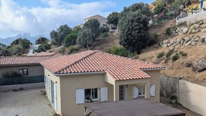 A residential property with a tiled roof, a covered patio with seating, and a view of surrounding hills and trees.